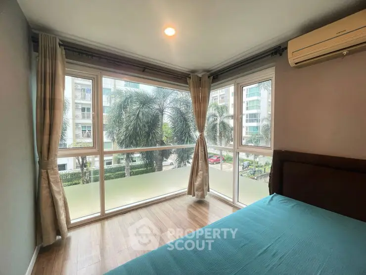 Spacious bedroom with large windows offering a lush garden view in modern apartment.