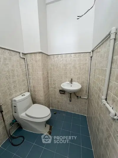 Compact bathroom with tiled walls and floor, featuring a toilet and small sink.