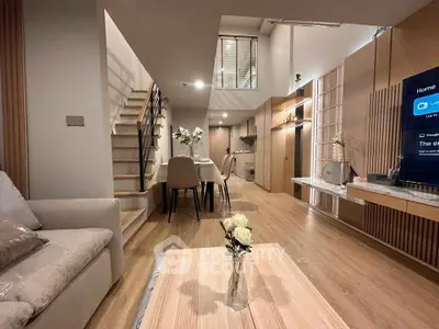 Modern duplex living room with open kitchen and stylish decor, featuring a cozy dining area and elegant staircase.
