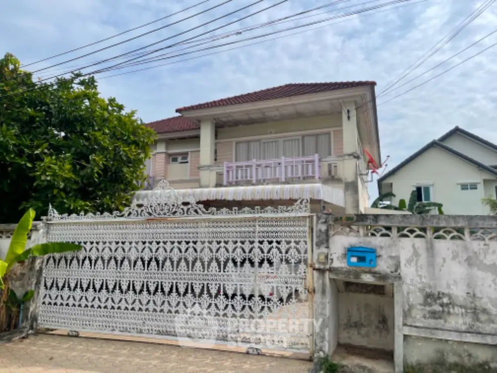 Charming two-story residence with a traditional design, featuring a spacious balcony and a secure ornate gate, set in a serene neighborhood.