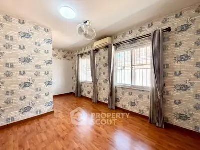 Spacious room with wooden flooring and patterned wallpaper, featuring large windows and air conditioning.