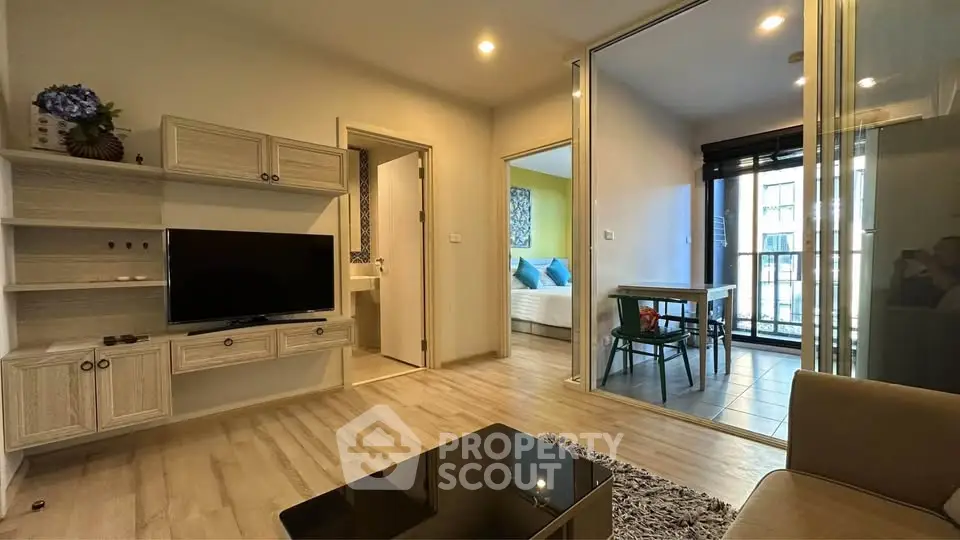 Modern living room with TV and glass doors leading to dining area in stylish apartment.