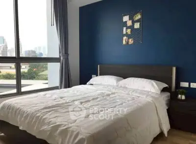 Modern bedroom with large window and stylish blue accent wall in urban apartment.