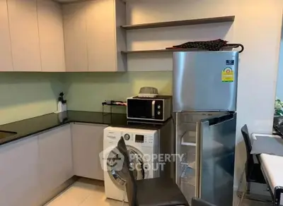 Modern kitchen with sleek cabinets, washing machine, and stainless steel fridge in a compact layout.