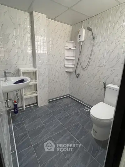 Modern bathroom with tiled walls, shower, and toilet in a sleek real estate property.