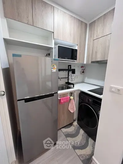Modern compact kitchen with fridge, microwave, and washing machine in stylish apartment.