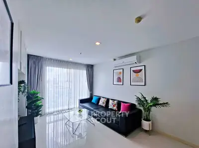 Modern living room with sleek black sofa, vibrant cushions, and stylish decor in a bright, airy space.