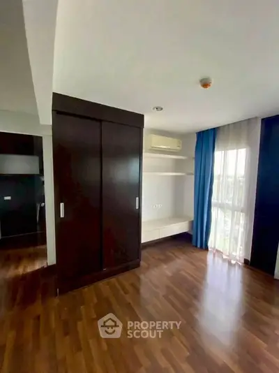 Spacious bedroom with wooden flooring and large window for natural light