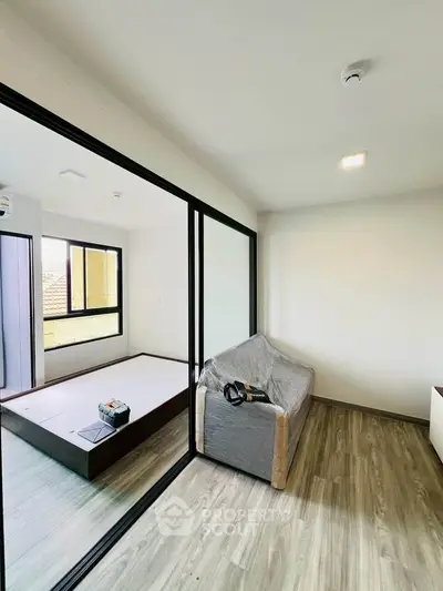 Modern apartment with glass partition and wooden flooring, featuring a cozy living area and natural light.