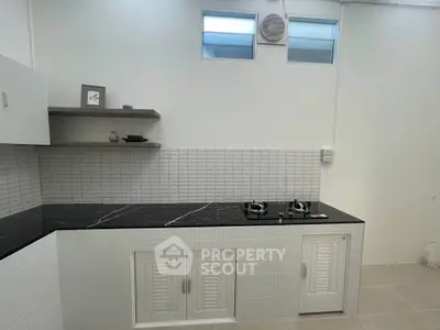 Modern kitchen with sleek black countertop and gas stove, featuring minimalist white cabinetry and tiled backsplash.