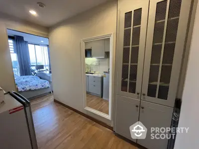 Modern apartment hallway with wooden flooring and built-in storage leading to a cozy bedroom with city view.