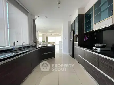 Spacious modern kitchen with sleek cabinetry and open layout leading to a bright living area.