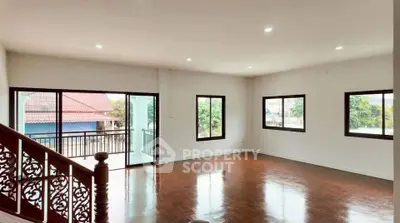 Spacious living room with wooden flooring and large windows offering natural light and balcony access.
