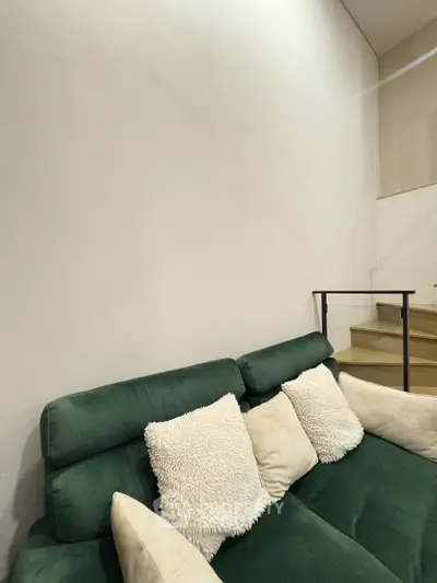 Modern living room with green sofa and cozy cushions near staircase