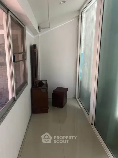 Narrow enclosed balcony with large windows and minimal furniture