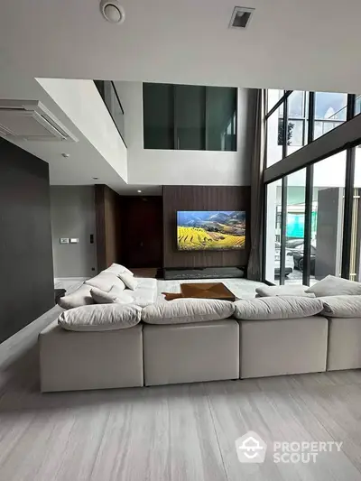 Luxurious modern living room with high ceilings and large windows, featuring a stylish sectional sofa and wall-mounted TV.