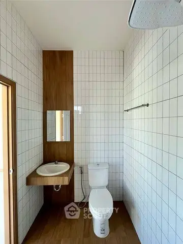 Modern minimalist bathroom with white tiles and wooden accents, featuring a sleek sink and toilet.