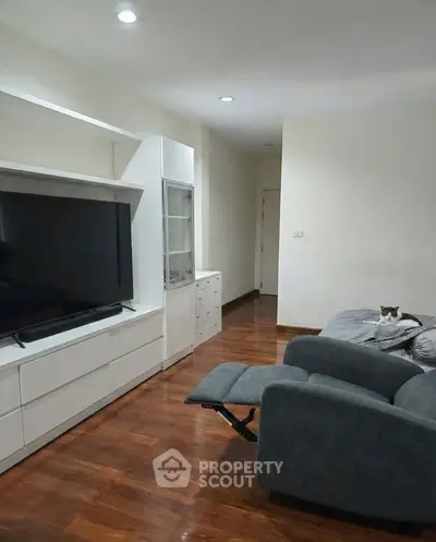 Spacious living room with modern TV unit and cozy seating on wooden flooring.