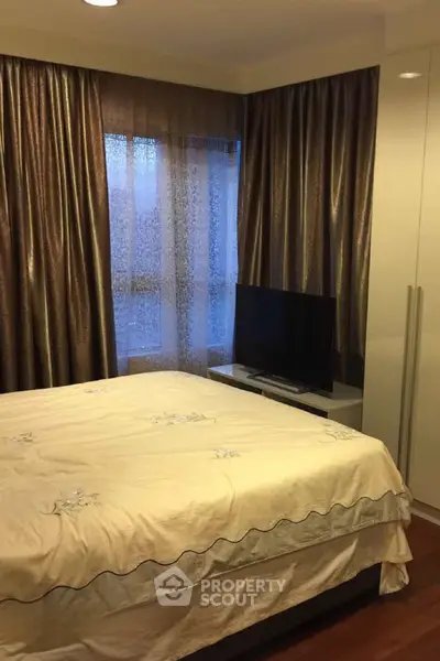 Cozy bedroom with elegant curtains and modern TV setup, perfect for relaxation.