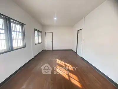 Spacious empty room with wooden flooring and large windows, ideal for customization.