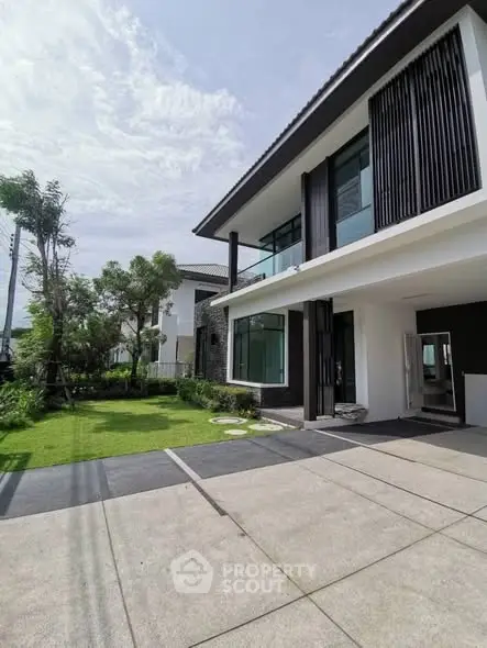 Modern two-story house with sleek design and spacious driveway, surrounded by lush greenery.