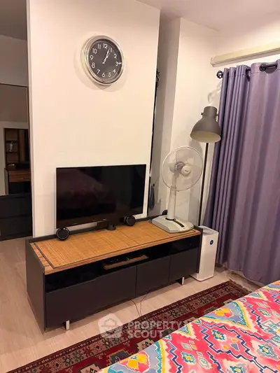 Cozy bedroom with modern decor, featuring a TV stand, fan, and stylish clock on the wall.