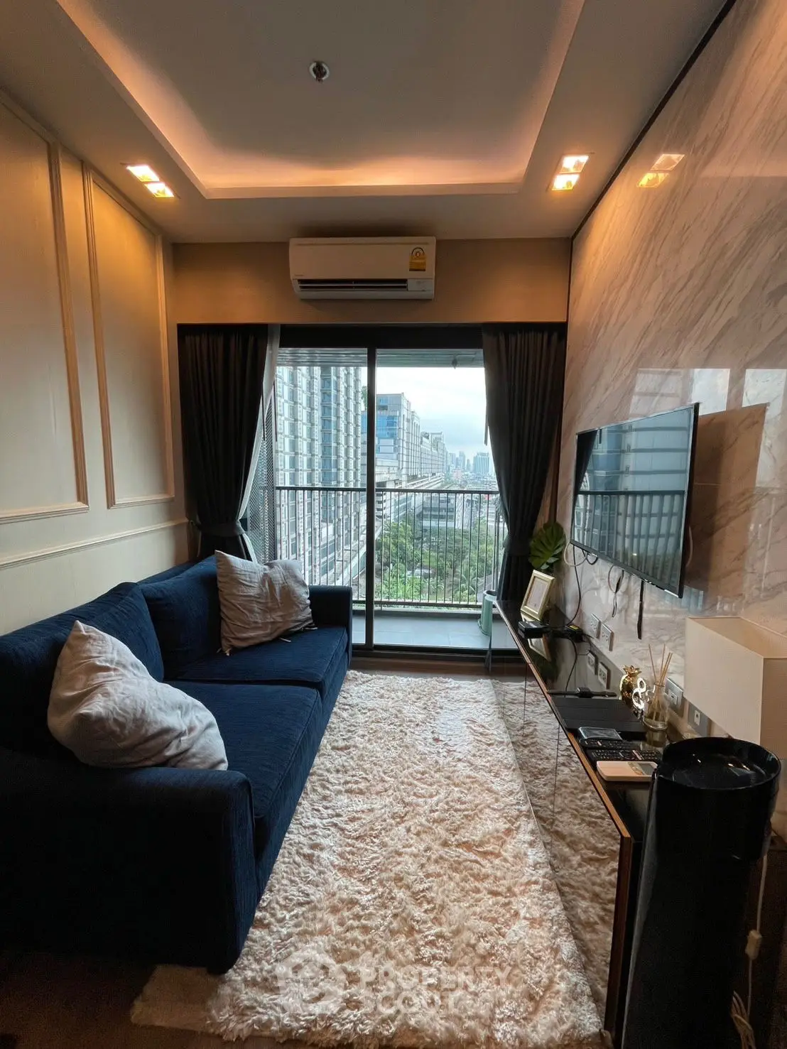 Chic living room with plush sofa, modern TV setup, and balcony view in urban apartment.