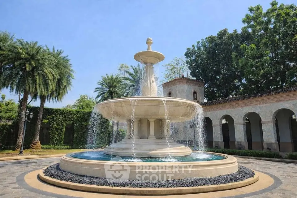 Elegant courtyard with a grand stone fountain surrounded by lush greenery and classic architecture.