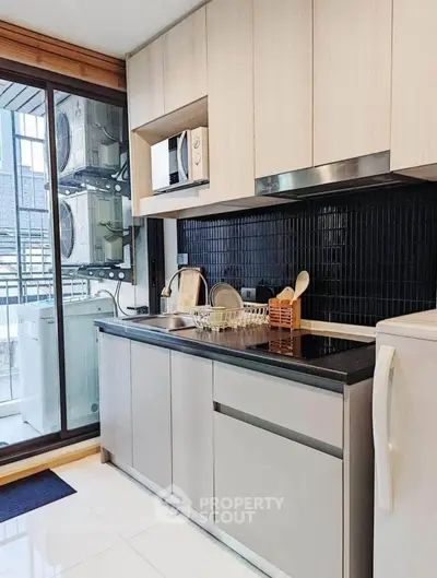 Modern kitchen with sleek cabinets and appliances, featuring a washing machine and microwave.