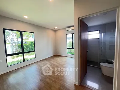 Spacious modern bedroom with ensuite bathroom and large windows overlooking garden.
