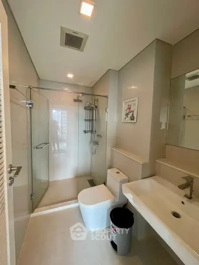 Modern bathroom with glass shower, sleek fixtures, and elegant decor in a contemporary apartment.