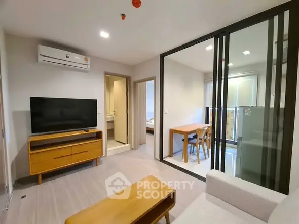 Modern living room with sleek furniture and glass partition leading to dining area.