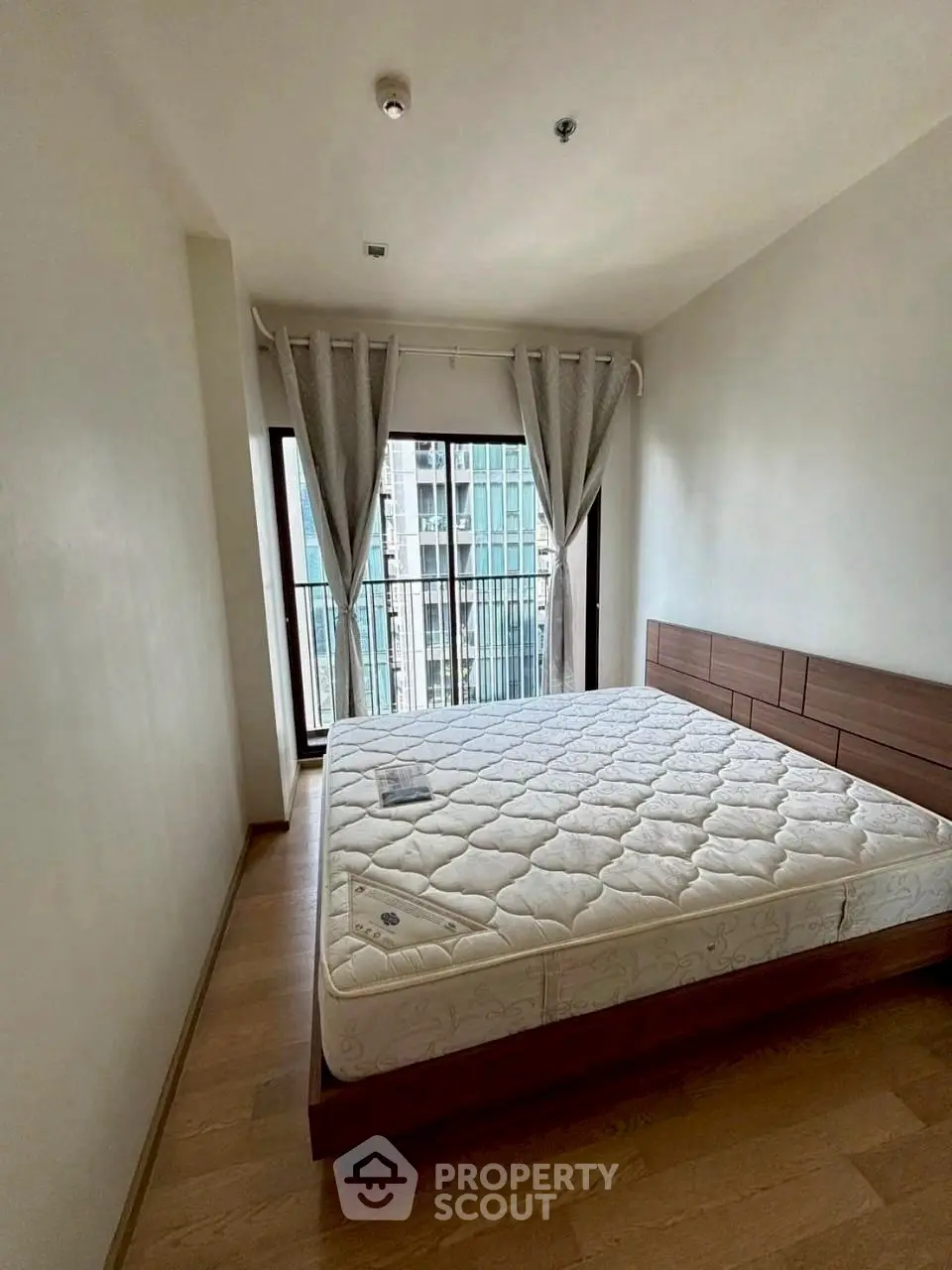 Spacious bedroom with large window and modern furnishings in high-rise apartment.