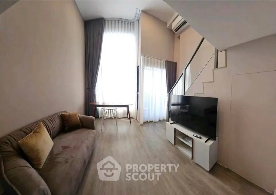 Modern living room with high ceiling and large windows, featuring a cozy sofa and flat-screen TV.