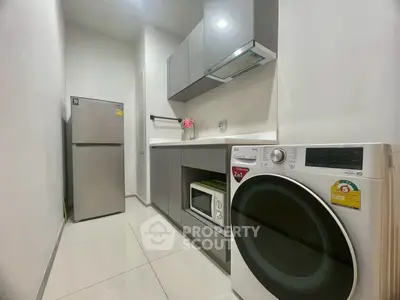 Modern kitchen with sleek appliances including fridge, washing machine, and microwave in a compact layout.