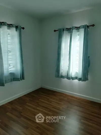 Bright empty room with wooden flooring and blue curtains