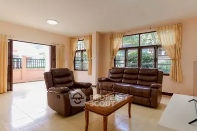 Spacious living room with leather sofas and large windows offering garden views.