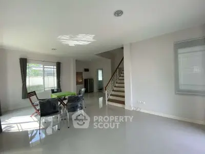 Spacious modern living room with dining area and staircase in bright natural light.