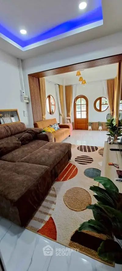 Spacious living room with modern decor and cozy seating area, featuring stylish lighting and vibrant rug.