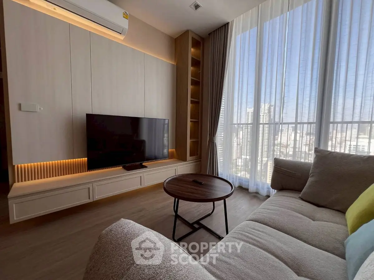 Modern living room with large window and city view, featuring cozy sofa and sleek TV setup.