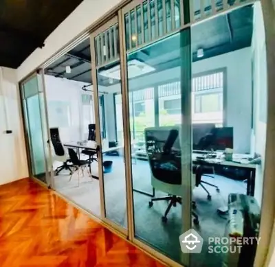 Sleek modern office space with glass partition walls and polished wooden floors, offering a professional yet inviting work environment.