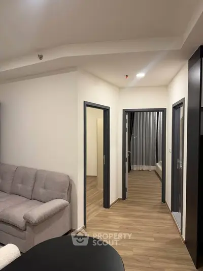 Modern apartment interior with cozy living room and hallway leading to bedrooms, featuring stylish decor and wood flooring.