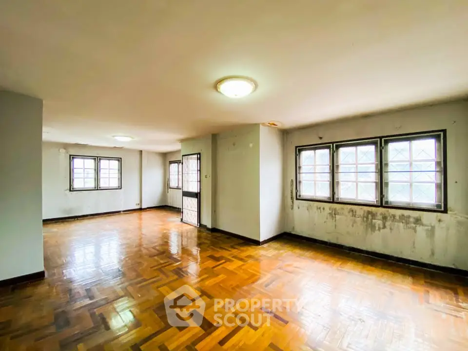 Spacious living room with parquet flooring and large windows offering natural light.