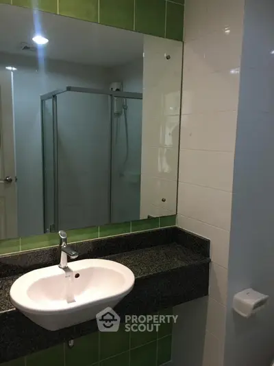 Modern bathroom with sleek sink and glass shower enclosure, featuring green and white tiles.