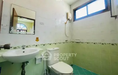 Charming bathroom with green tiles and modern fixtures, featuring a window for natural light.