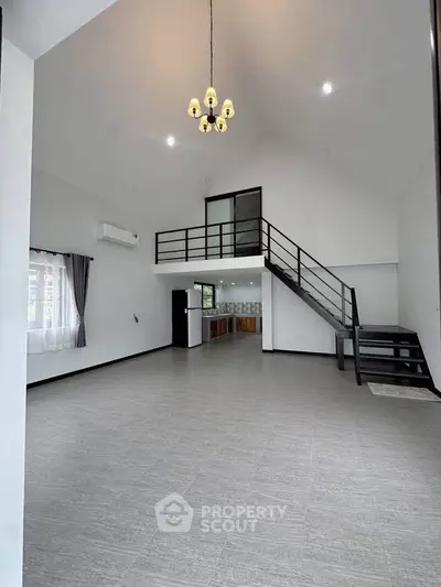 Spacious modern living room with high ceiling and loft, featuring sleek staircase and open kitchen layout.