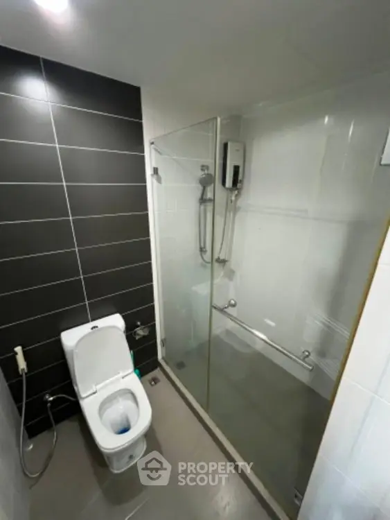 Modern bathroom with sleek black and white tiles, glass shower enclosure, and contemporary toilet.