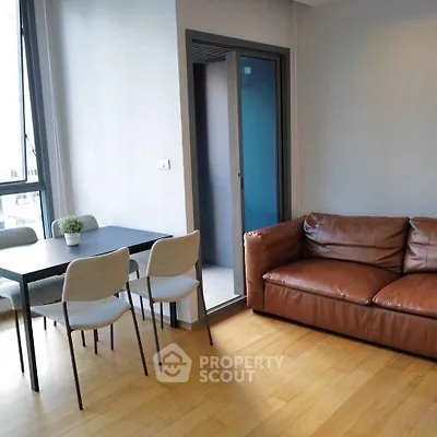Modern living room with leather sofa and dining area, featuring sleek design and natural light.