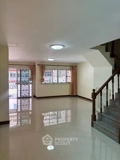 Spacious living room with glossy tiled floors and staircase, ideal for modern family living.