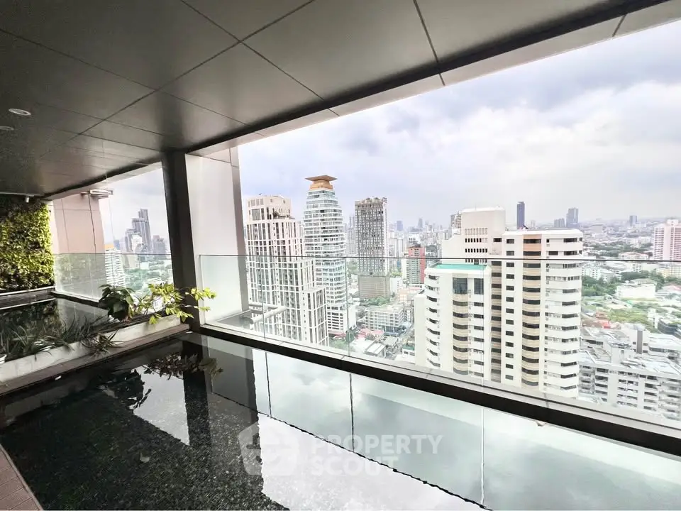 Stunning city view from a high-rise balcony with glass railing and lush greenery.